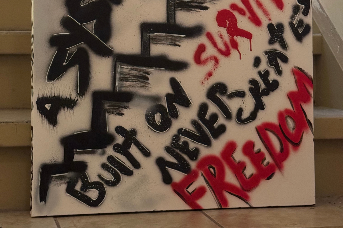 Close-up of OBAY DI DREAM's "A System Built on Survival Never Creates Freedom," showing layered spray-paint texture, white hand-drawn outlines, red drips, and the hand-lettered side edge.