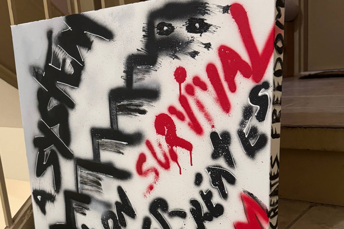 Close-up of OBAY DI DREAM's "A System Built on Survival Never Creates Freedom," showing layered spray-paint texture, white hand-drawn outlines, red drips, and the hand-lettered side edge.